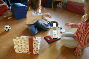 die Mädchen betrachten ihren Turm aus Messbecher und zwei Wassrwaagen auf der Elektrowaage